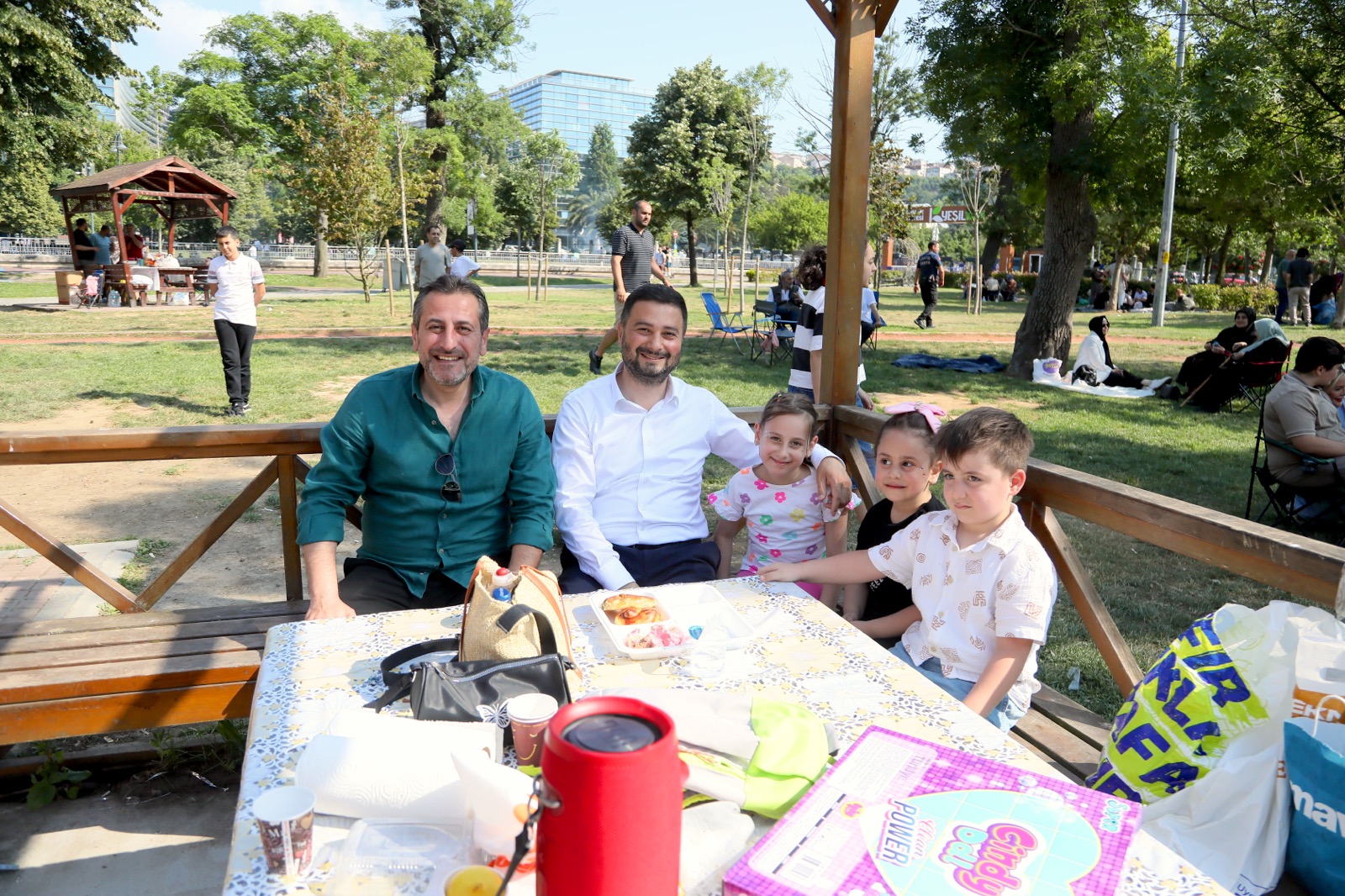 Mevlüt Öztekin parkta bir piknik masasında bir adam ve üç çocukla birlikte oturuyor.