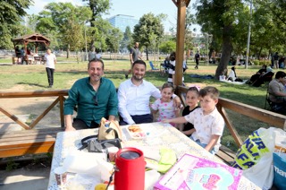 Mevlüt Öztekin parkta bir piknik masasında bir adam ve üç çocukla birlikte oturuyor.