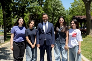 Mevlüt Öztekin parkta taş döşeli yolda dört genç kızın ortasında poz veriyor.