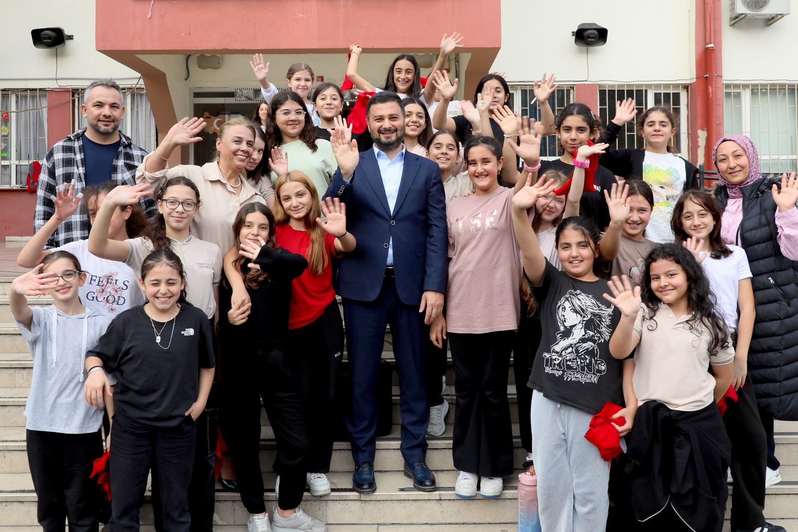 Mevlüt Öztekin okul merdivenlerinde el sallayan öğrencilerin ortasında duruyor.