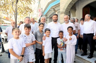 Mevlüt Öztekin taş kemerli bir girişin önünde çocuklar ve yetişkinlerden oluşan kalabalık bir grupla poz veriyor.