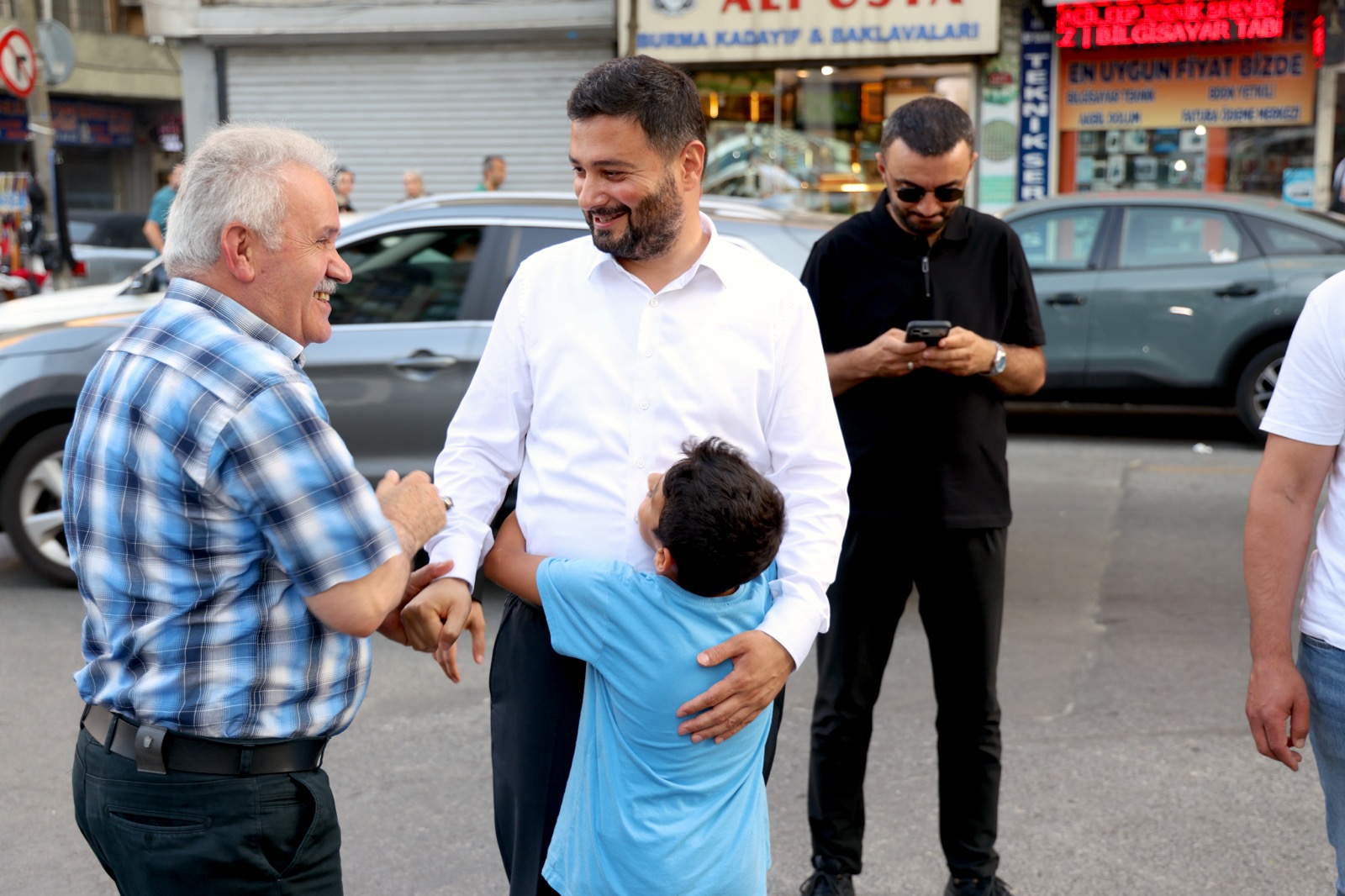 Mevlüt Öztekin caddede kendisine sarılan bir çocuğu kucaklarken yaşlı bir hemşehrimizle gülüşüyor.