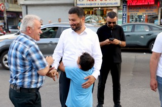 Mevlüt Öztekin caddede kendisine sarılan bir çocuğu kucaklarken yaşlı bir hemşehrimizle gülüşüyor.