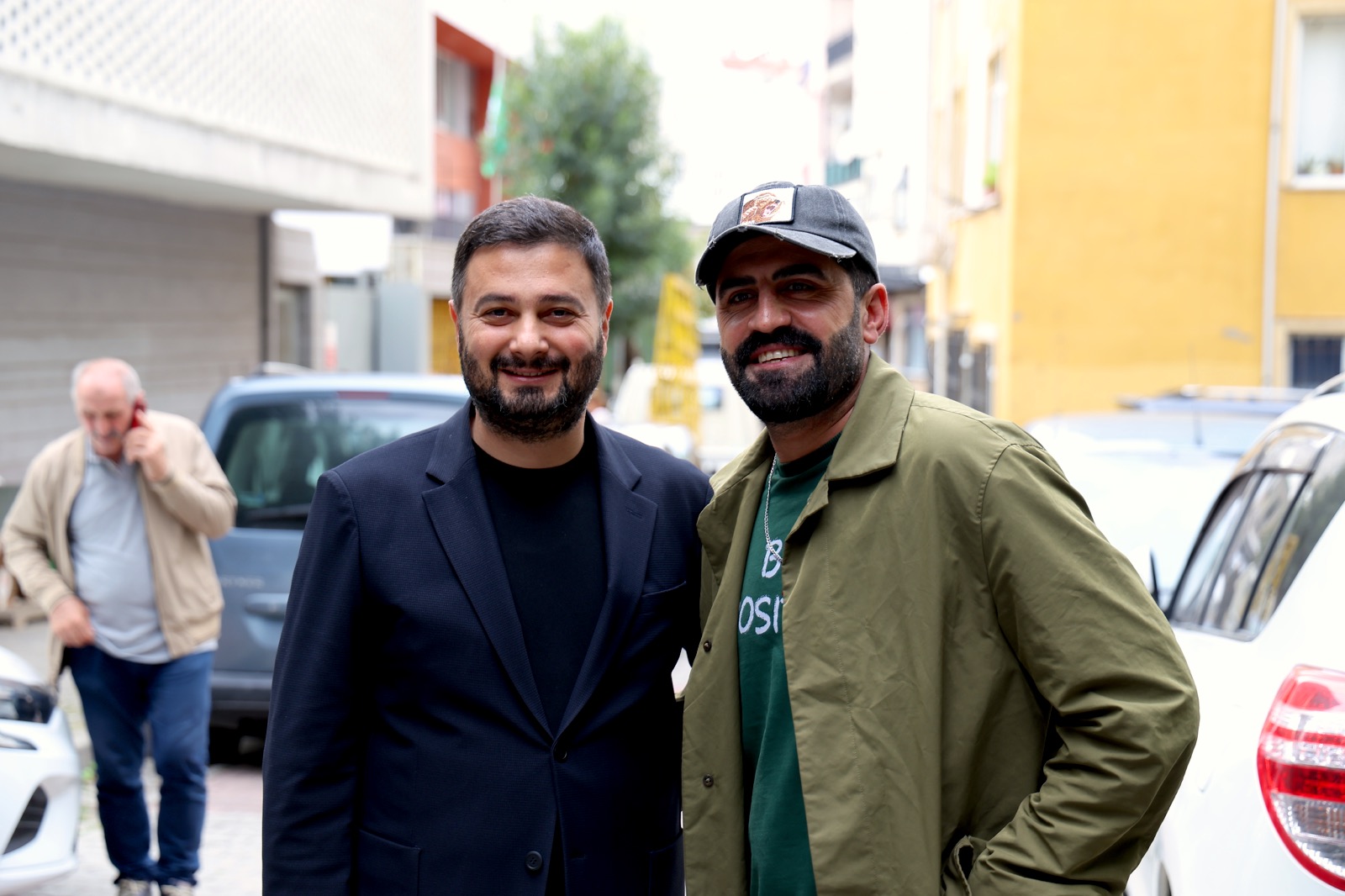 Mevlüt Öztekin park etmiş arabaların arasında şapkalı, sakallı bir hemşehrimizle yan yana gülümsüyor.