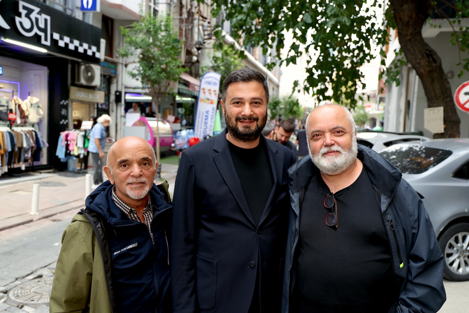 Mevlüt Öztekin dükkânların sıralandığı bir sokakta iki yaşlı hemşehrimizle yan yana poz veriyor.