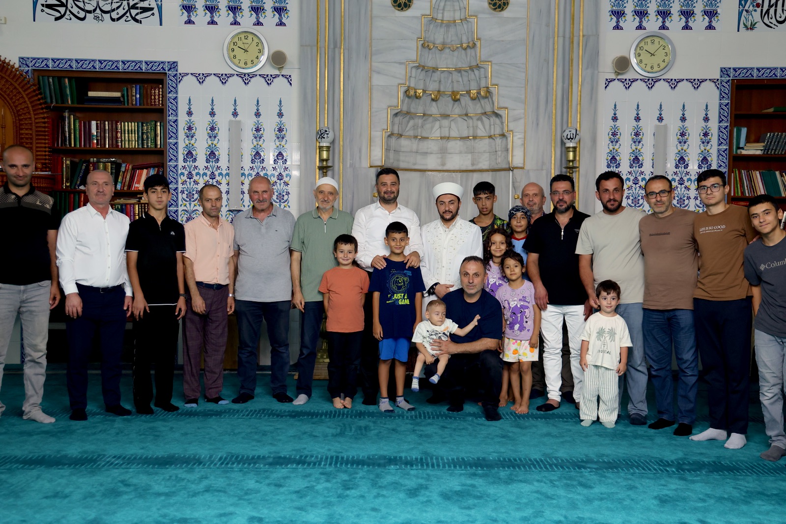 Mevlüt Öztekin bir caminin mihrabı önünde imam, cemaat ve çocuklarla toplu fotoğrafta duruyor.