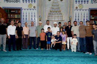 Mevlüt Öztekin bir caminin mihrabı önünde imam, cemaat ve çocuklarla toplu fotoğrafta duruyor.