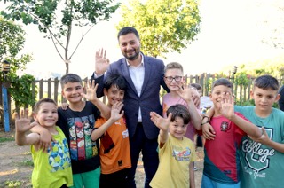 Mevlüt Öztekin bir bahçede el sallayarak gülen yedi çocuğun ortasında, o da el sallıyor.